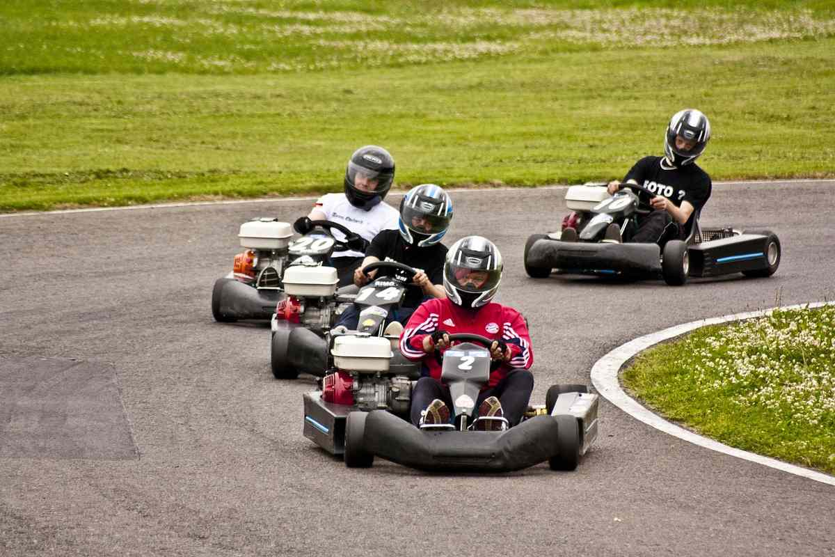 Quatre pilotes en karting sur une piste courbe, casques, numéros, moteur visible