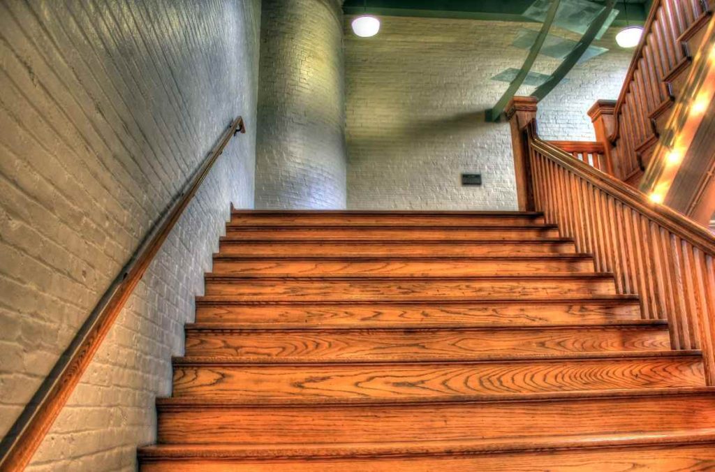Un escalier en bois avec main-courante et éclairage dans un couloir en brique