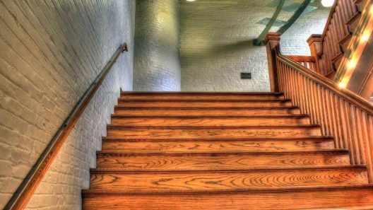 Un escalier en bois avec main-courante et éclairage dans un couloir en brique