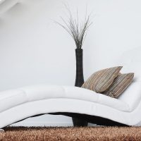 Une chaise longue blanche avec coussins, vase et plante sur tapis