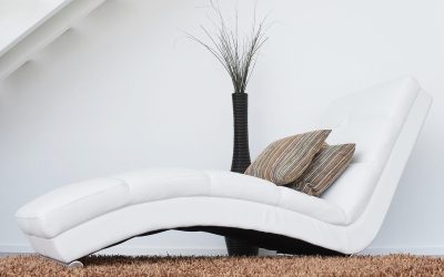 Une chaise longue blanche avec coussins, vase et plante sur tapis